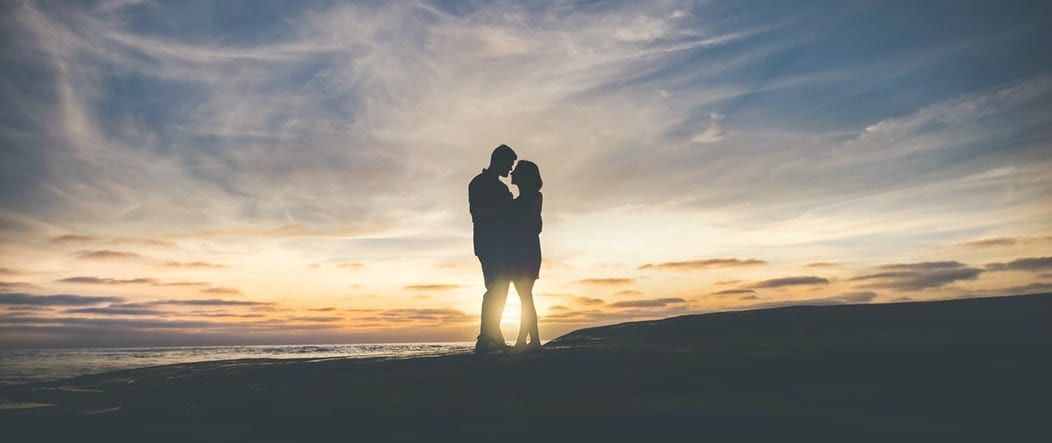 a man and a woman are kissing on the beach at sunset .