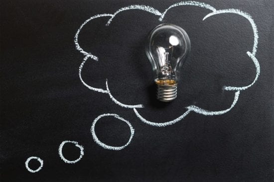 a light bulb is sitting inside of a thought bubble drawn on a blackboard .