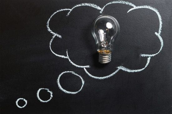 a light bulb is sitting inside of a thought bubble drawn on a blackboard .