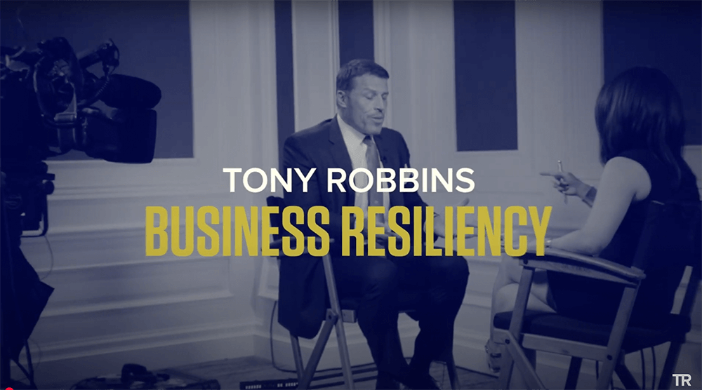 a man in a suit and tie sits in front of a camera with the words tony robbins business resiliency above him