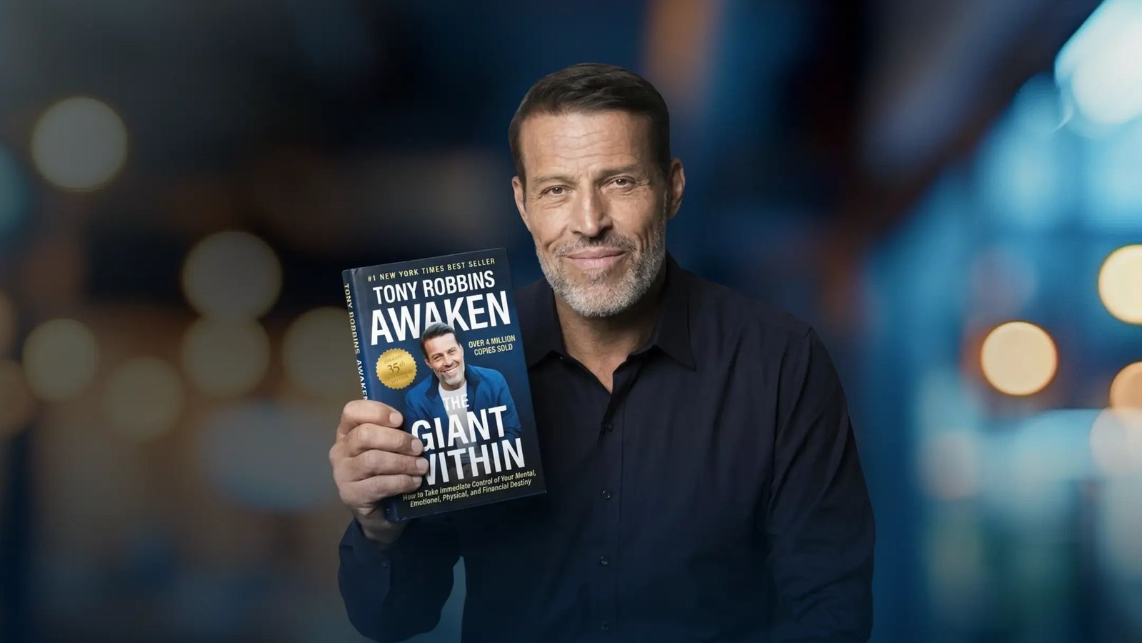 Tony Robbins holding his book "Awaken the Giant Within".