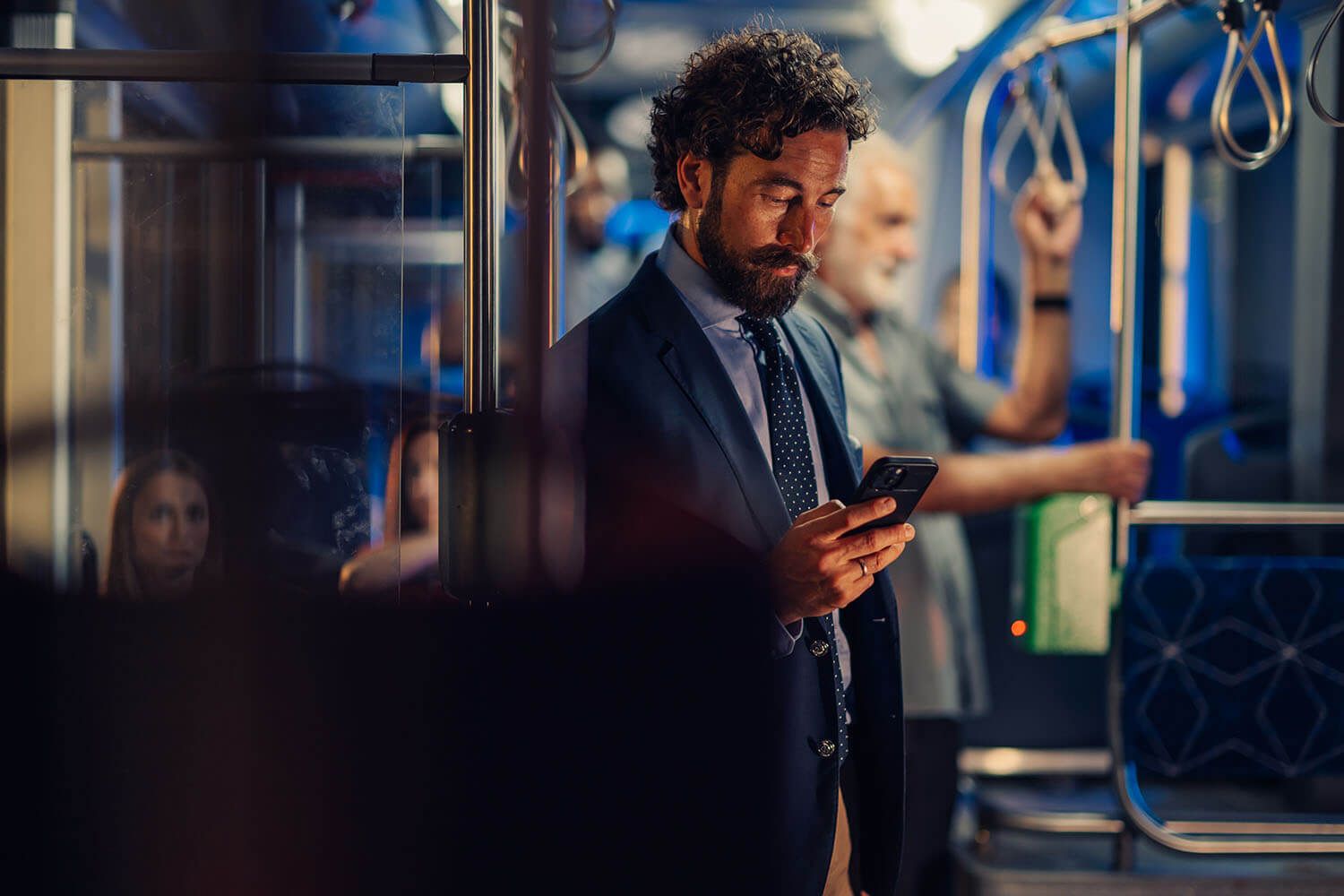 A man in a suit looks at his phone while standing on a bus.
