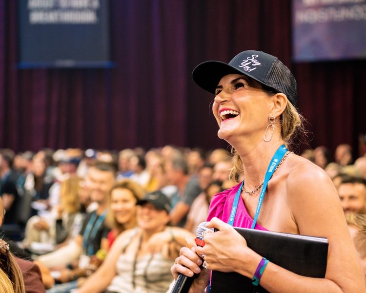 a woman is laughing while holding a microphone in front of a crowd .