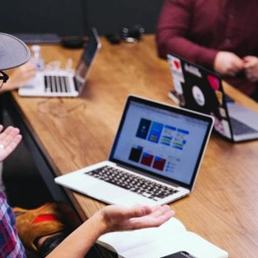 a group of people are sitting at a table with laptops .