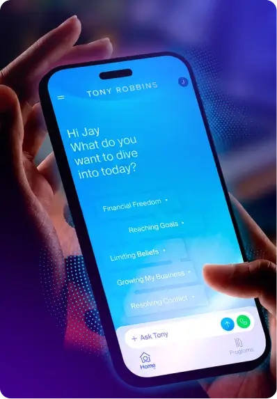 Hand holding a smartphone displaying the Tony Robbins app with a welcome message and coaching topic options.