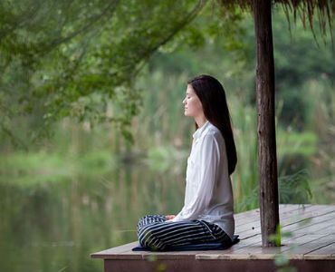 a woman is sitting on a wooden dock with her eyes closed .