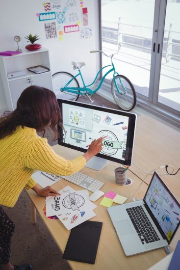 a woman is sitting at a desk using a computer and a laptop .