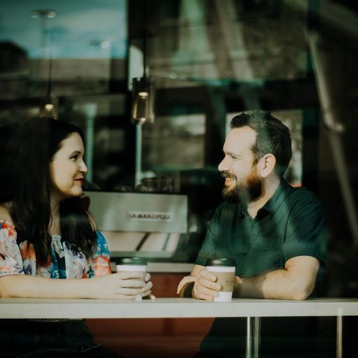 a man and a woman are sitting at a table in a cafe looking at each other .