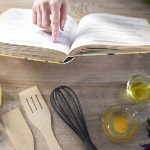 a woman is reading a cookbook on a wooden table .