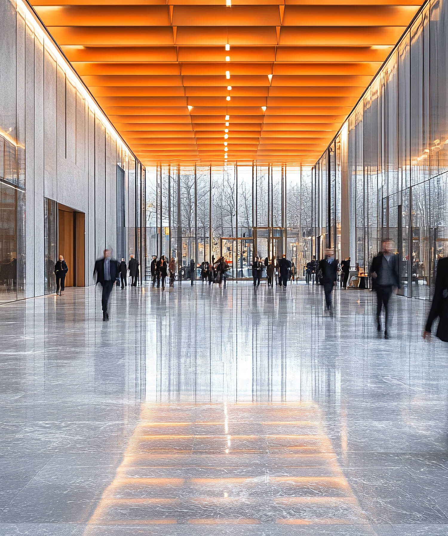 A modern, brightly lit hallway with an orange paneled ceiling, reflective grey marble floor, and blurred people walking.