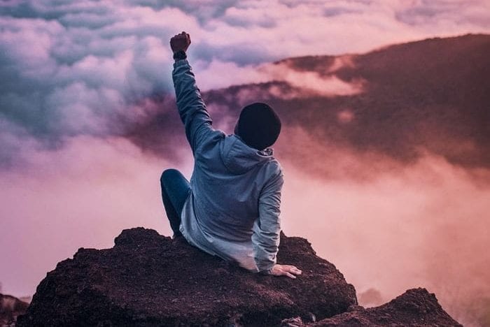 a man is sitting on top of a rock with his fist in the air .