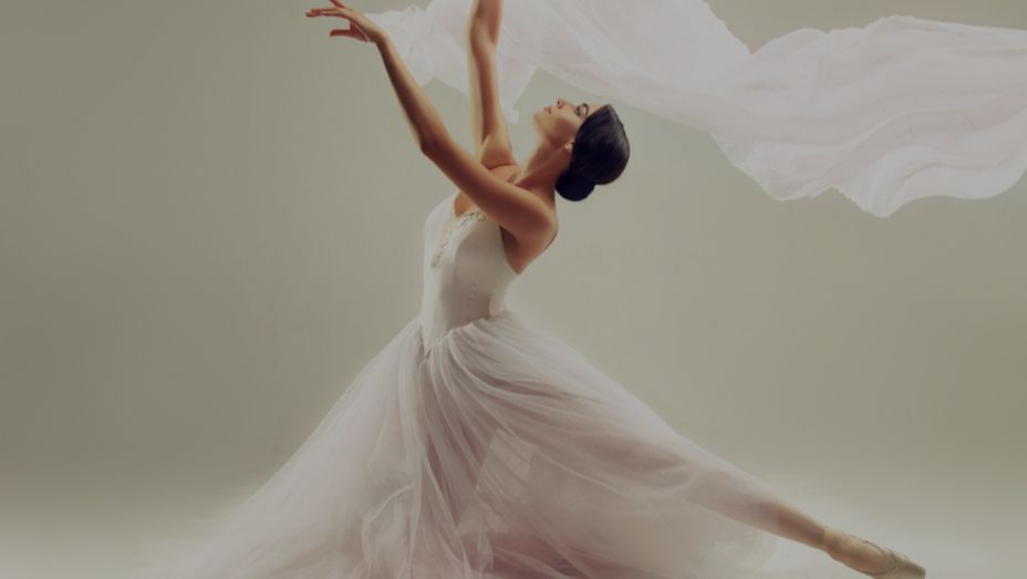 a ballerina in a white dress is dancing with a white cloth flying in the air .