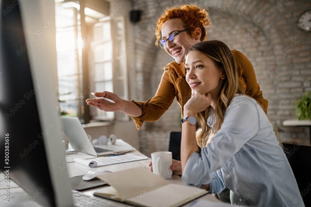 two women are looking at a computer screen together in an office .