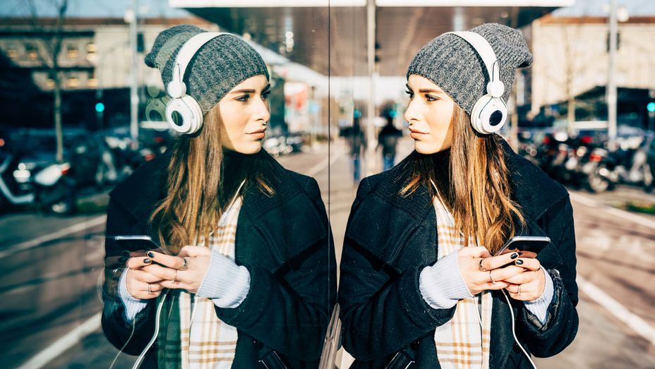 a woman wearing headphones and a beanie is looking at her phone .