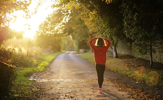 a woman is walking down a dirt road at sunset .