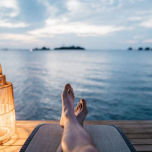a person is laying on a dock with their feet up in front of the ocean .