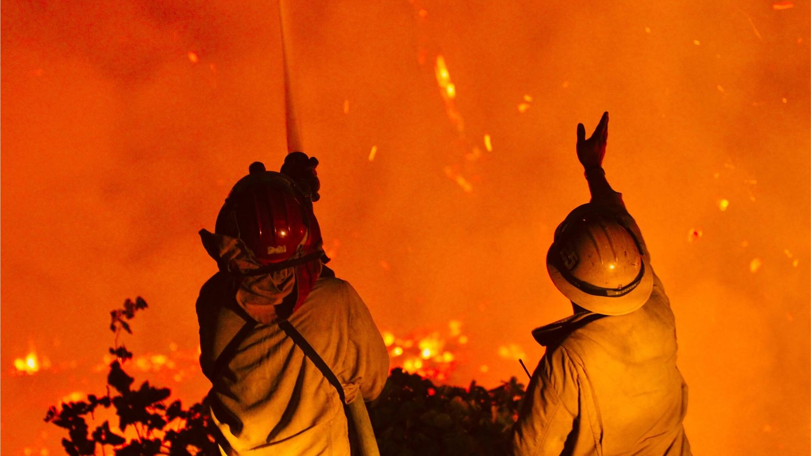 two firefighters are standing in front of a large fire .