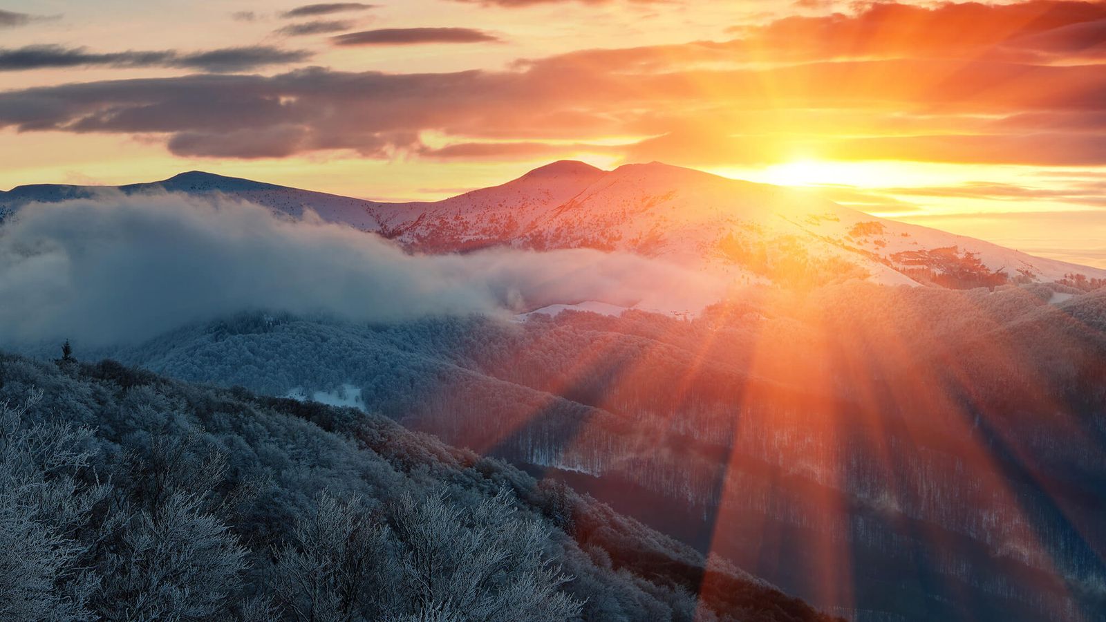Vibrant sunset with sun rays over snow-covered mountains and frosted trees.