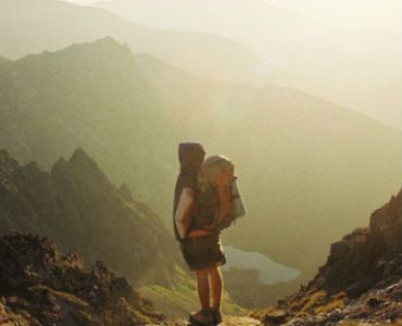 a person with a backpack is standing on top of a mountain .