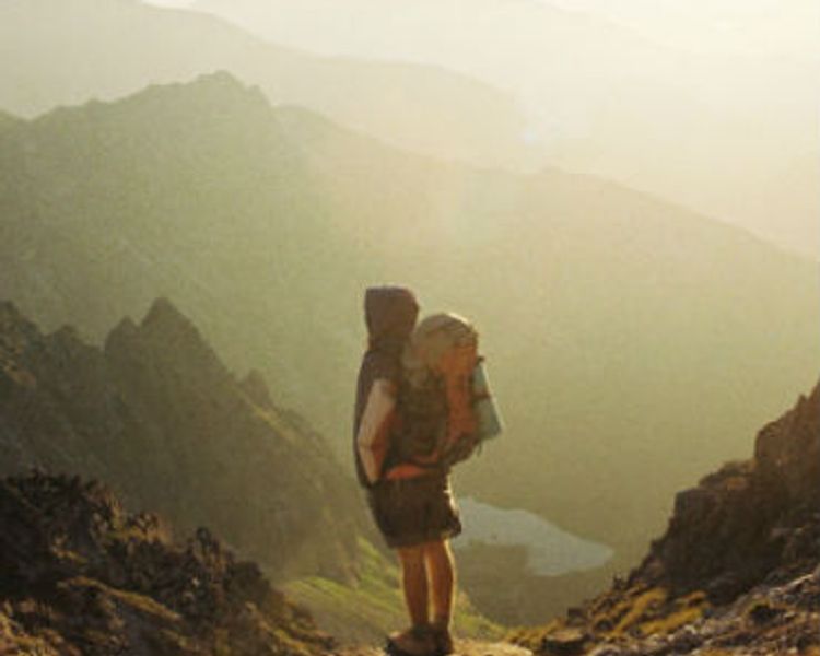 a person with a backpack is standing on top of a mountain .