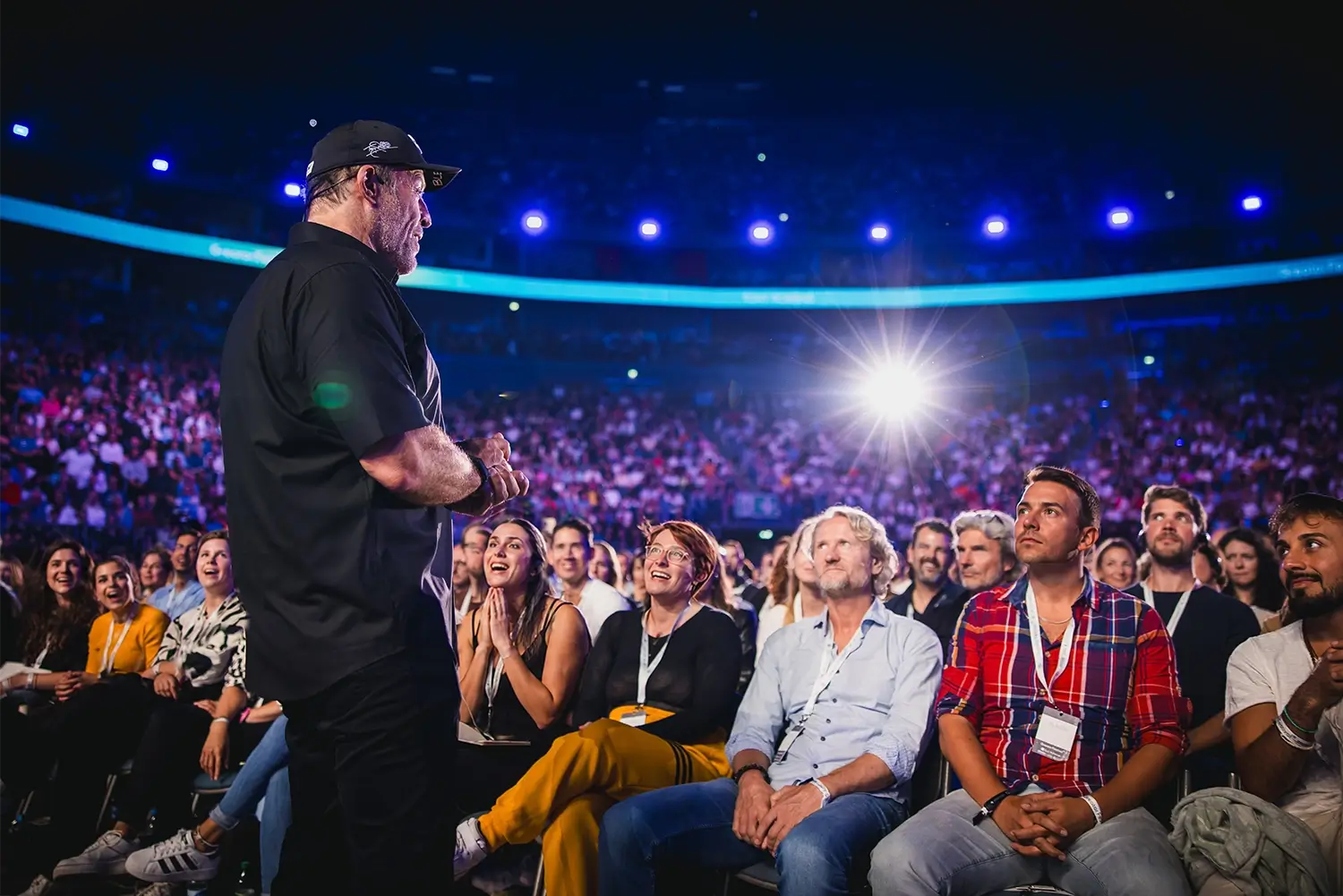 Speaker on stage addressing a large, attentive audience in an arena.