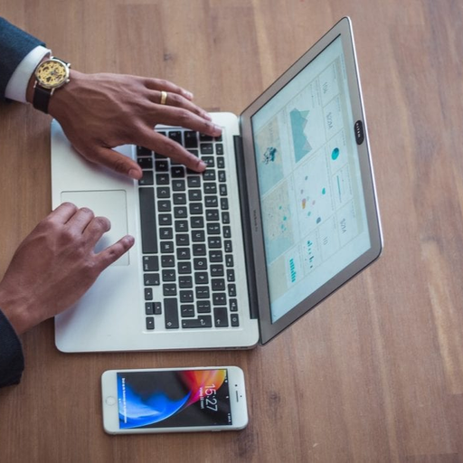 a man is typing on a laptop next to a cell phone that says 12:37