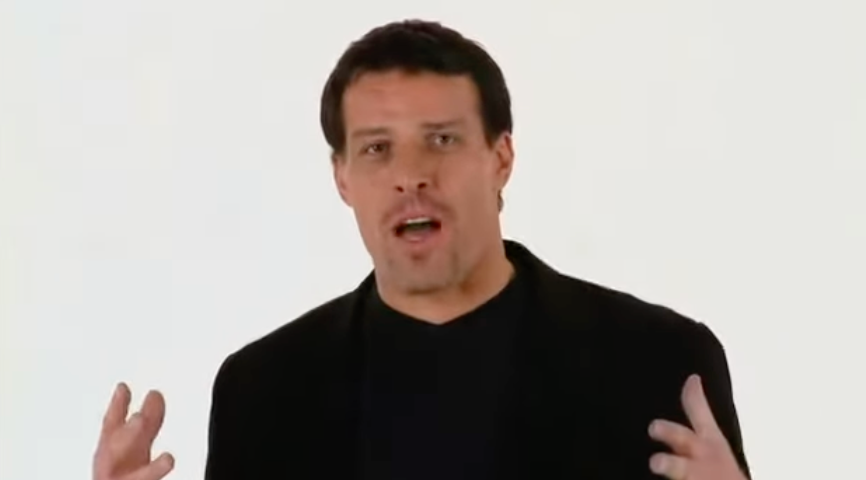 a man in a black jacket and black shirt is talking with his hands outstretched .