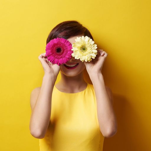 a woman in a yellow dress is holding two flowers in front of her eyes .