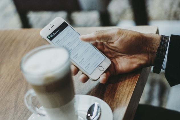 a person is holding a cell phone in their hand next to a cup of coffee .