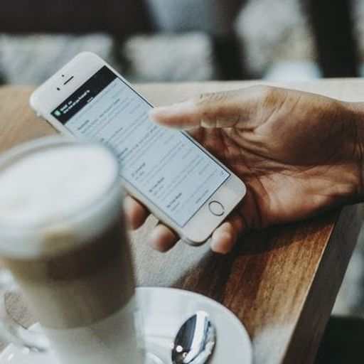 a person is holding a cell phone in their hand next to a cup of coffee .