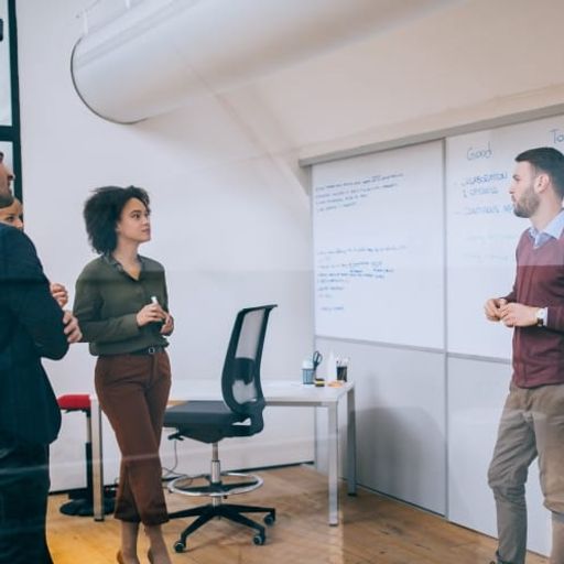 a group of people are standing in front of a whiteboard in an office .