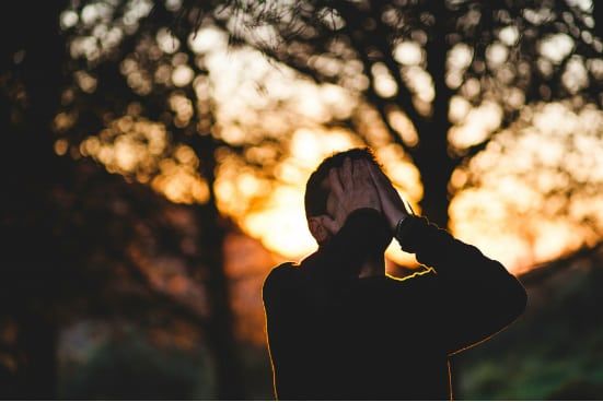 a man is covering his face with his hands in front of a sunset .