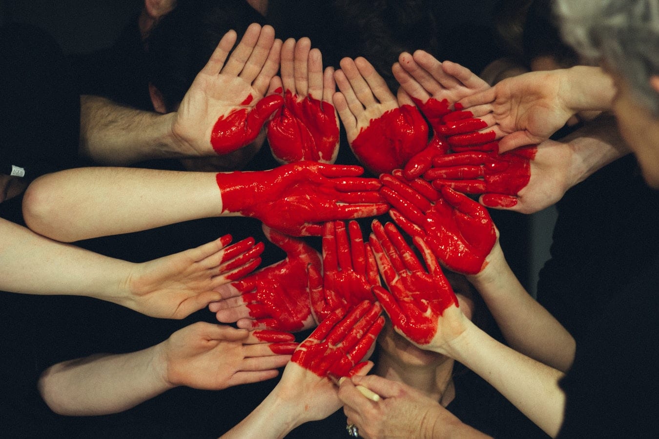 a group of people are making a heart with their hands painted red .