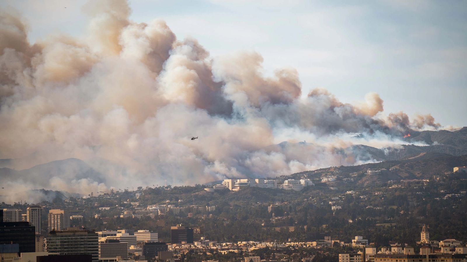 a large cloud of smoke is coming out of a mountain over a city .