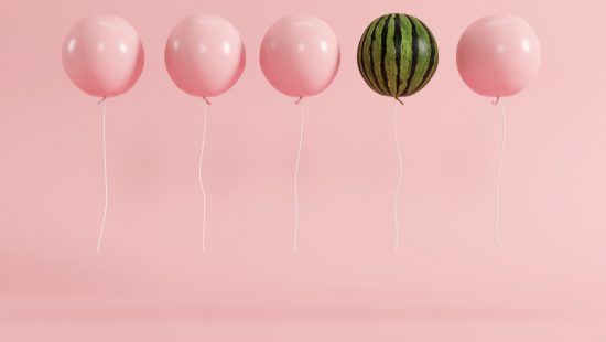 a watermelon is floating in the air next to a row of pink balloons .