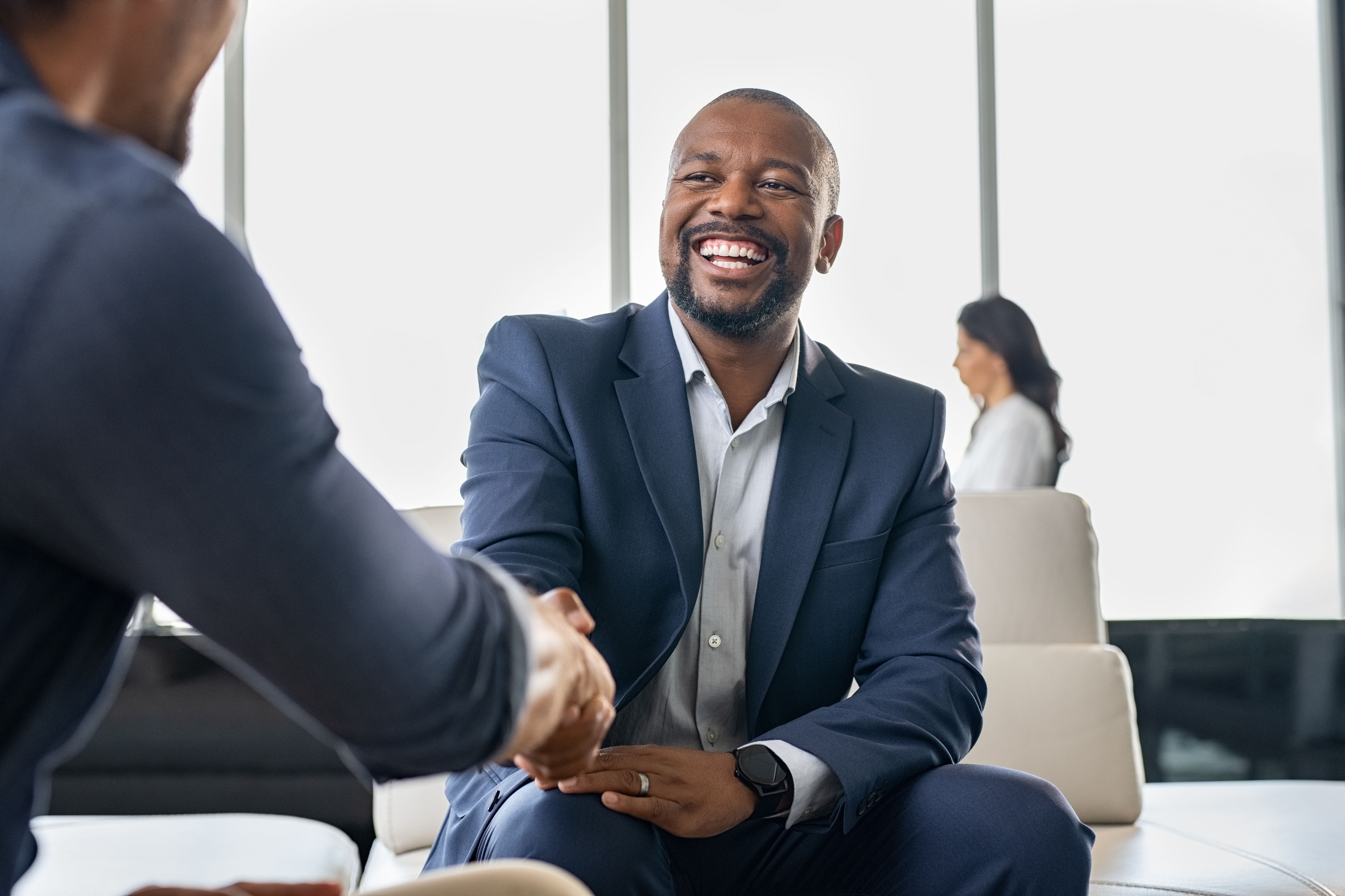 a man in a suit is shaking hands with another man while sitting on a couch .