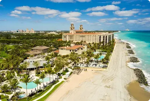 Aerial view of a grand beachfront resort with pools, palm trees, and a turquoise ocean.