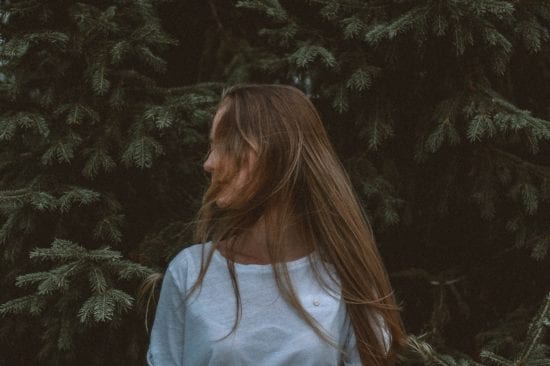 a woman with long hair is standing in front of a tree .