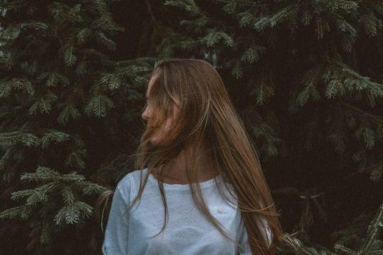a woman with long hair is standing in front of a tree .