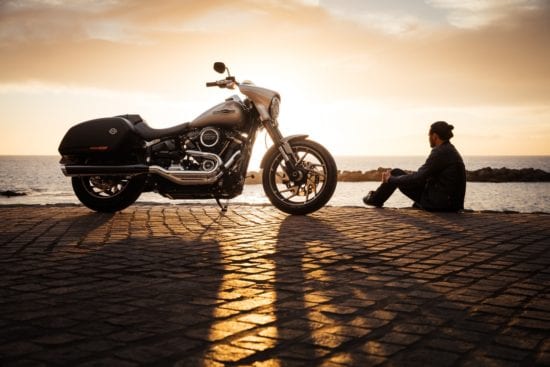 a man is sitting on the sidewalk next to a motorcycle .