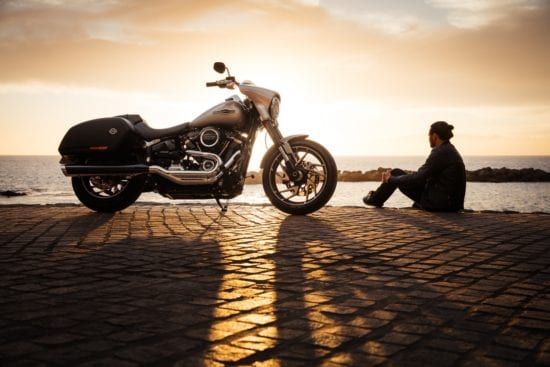 a man is sitting on the sidewalk next to a motorcycle .