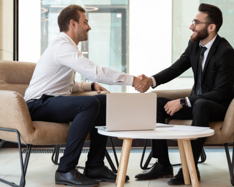two men are shaking hands while sitting on a couch
