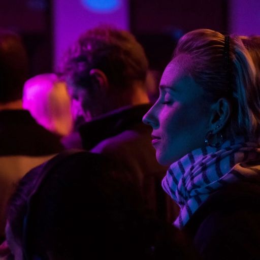 a woman is sitting in a crowd of people at a concert with her eyes closed .