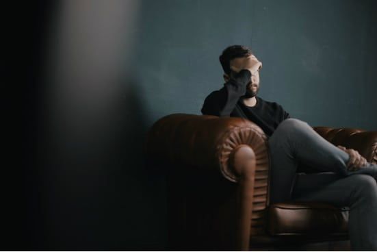 a man is sitting on a couch with his head in his hand .
