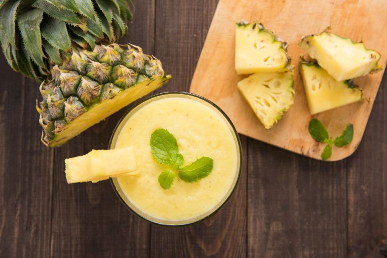 a pineapple smoothie in a glass next to pineapple slices on a wooden table .
