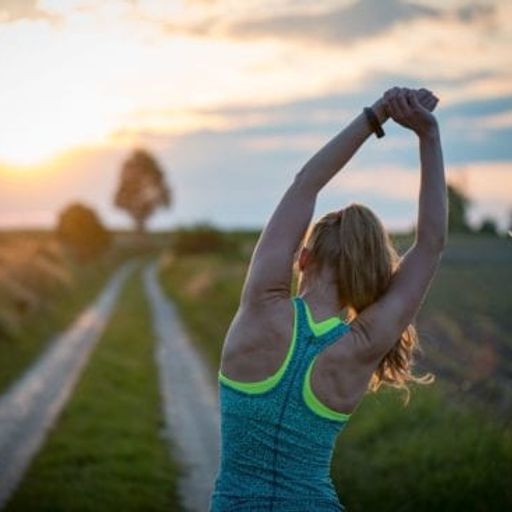 a woman is stretching her arms on a dirt road at sunset .