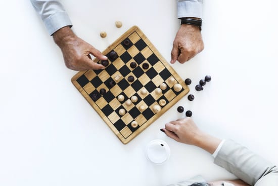 a man and a woman are playing a game of checkers on a chess board .