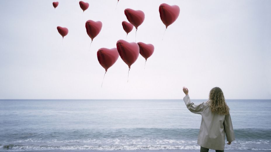 a woman is standing on the beach throwing heart shaped balloons into the air .
