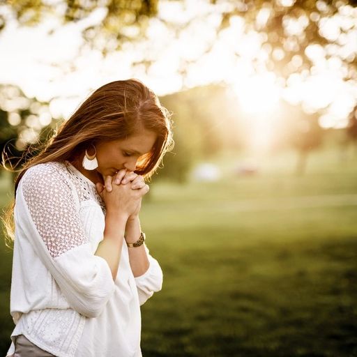 a woman is praying in a park with her hands folded .