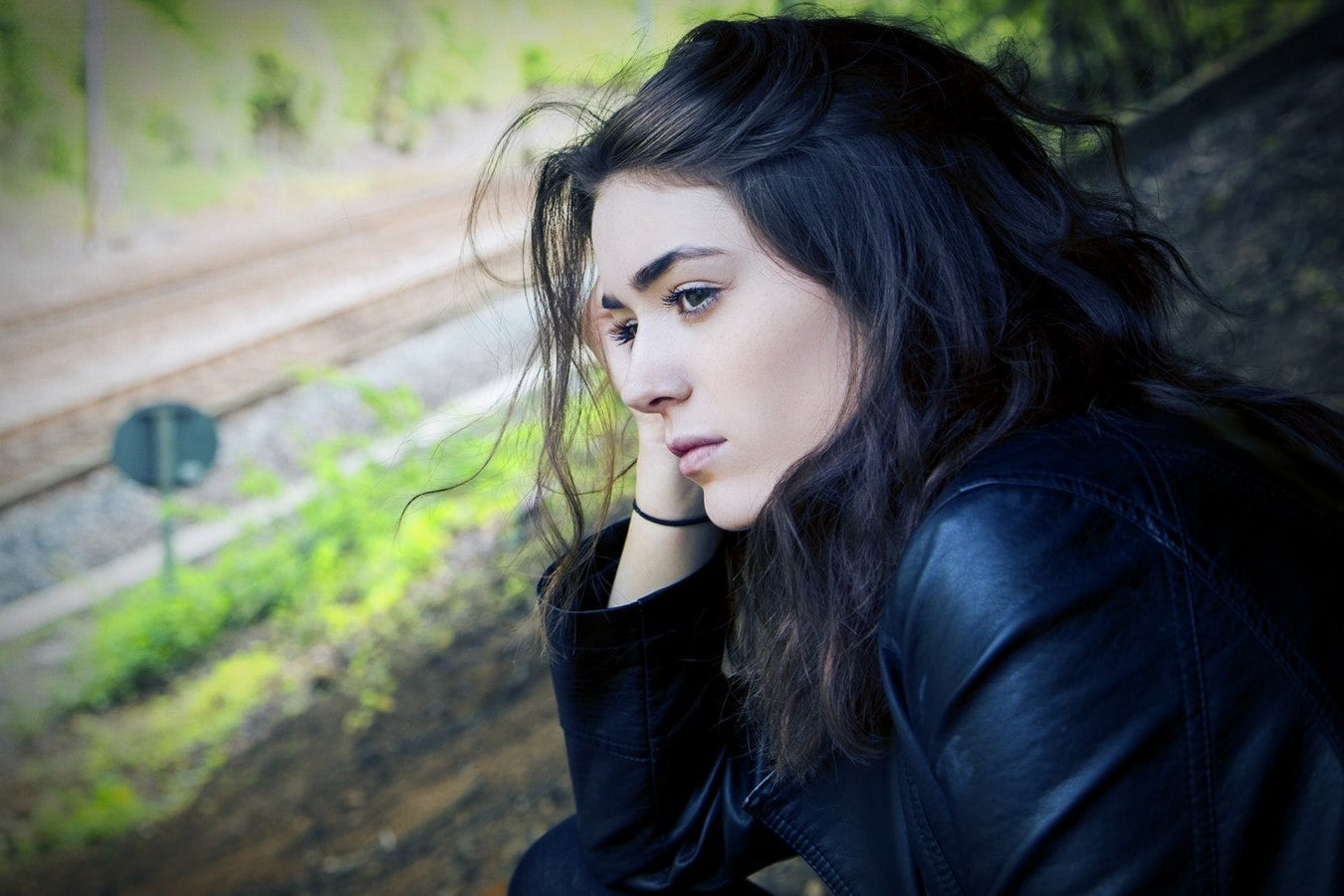 a woman in a black jacket is sitting on the ground with her head resting on her hand .
